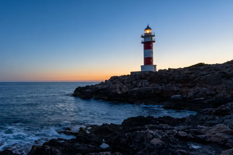Faro a strisce rosse e bianche su una scogliera al tramonto